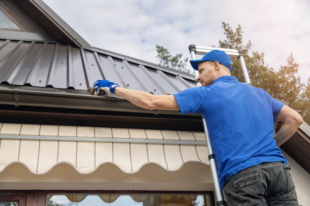 Service technician removing debris during gutter cleaning on a residential roof in Florence, Alabama.
